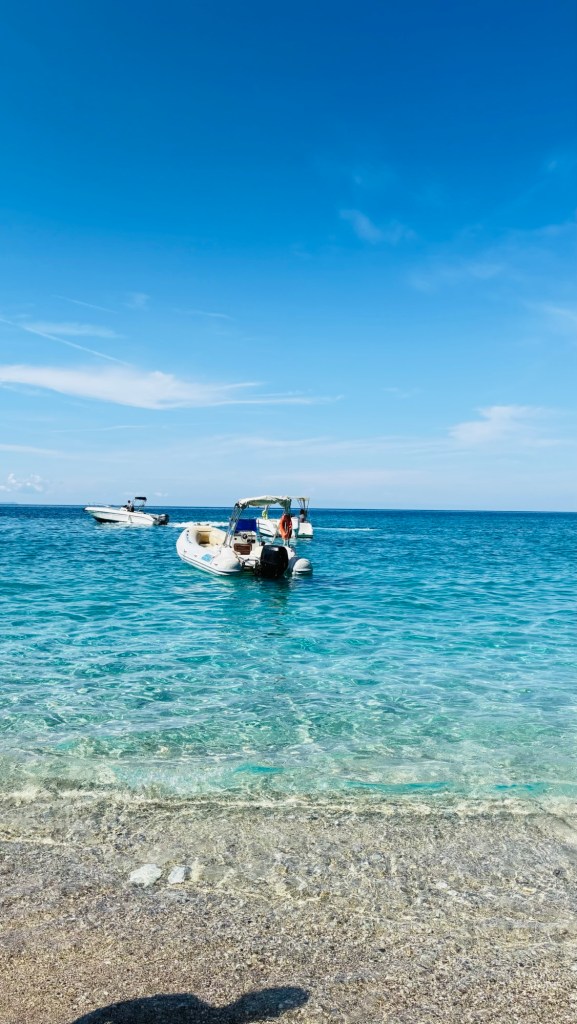 Un bateau à moteur sur une mer turquoise sous un ciel bleu, avec une plage en premier plan.