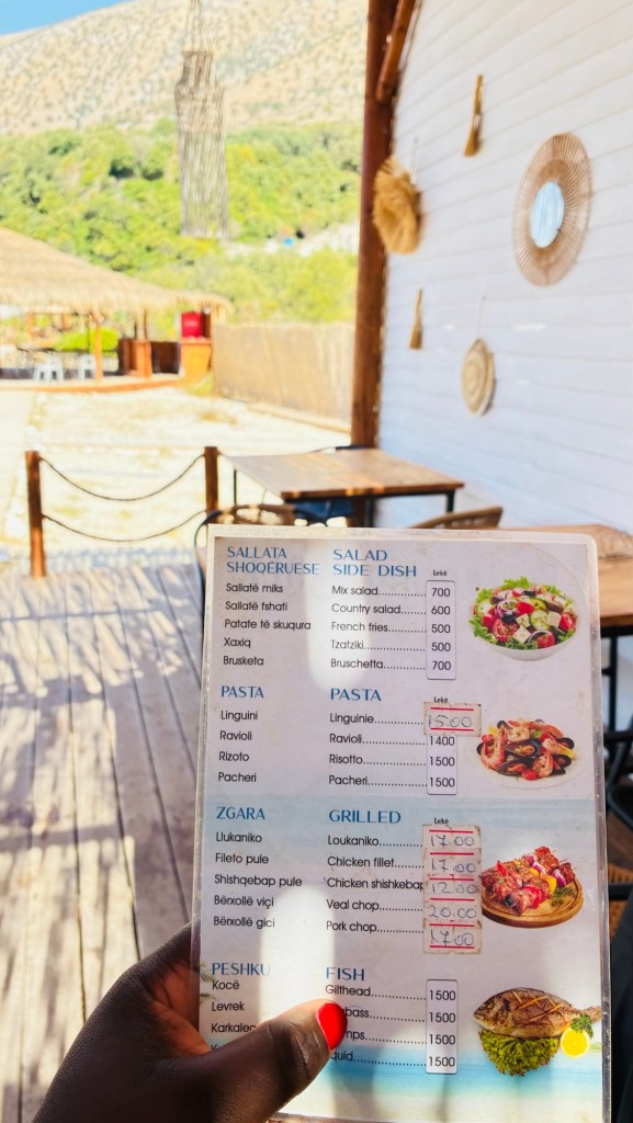 Menu de restaurant affichant des plats de salades, pâtes, grillades et poissons, avec les prix en lek, dans un environnement extérieur ensoleillé.