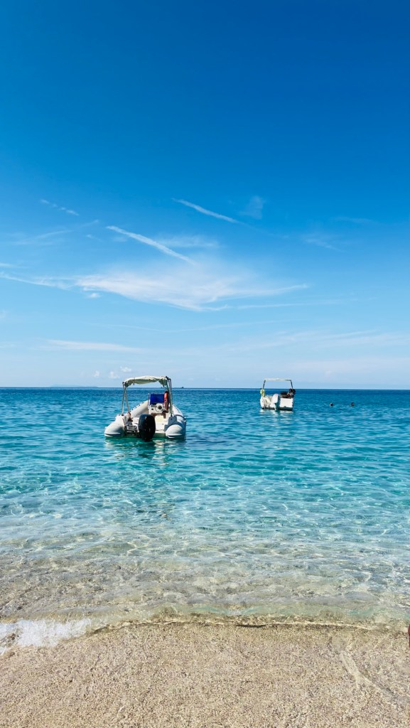 Deux bateaux à moteur flottent sur une mer turquoise calme, avec un ciel bleu dégagé en arrière-plan.