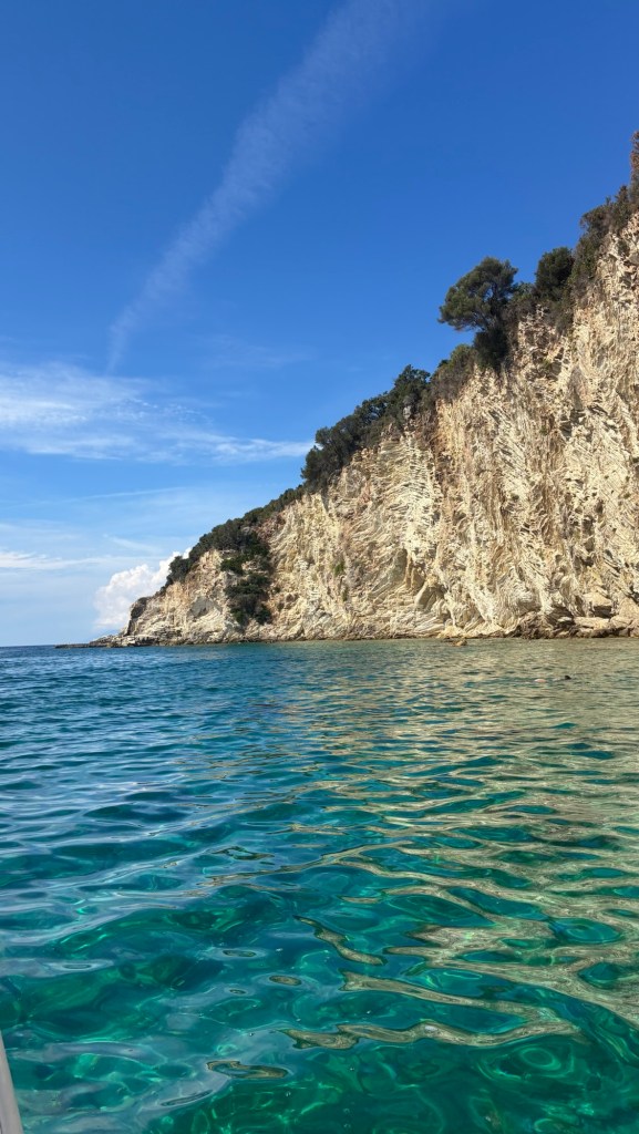 Vue d'une côte rocheuse sous un ciel bleu, avec des eaux claires et turquoises.
