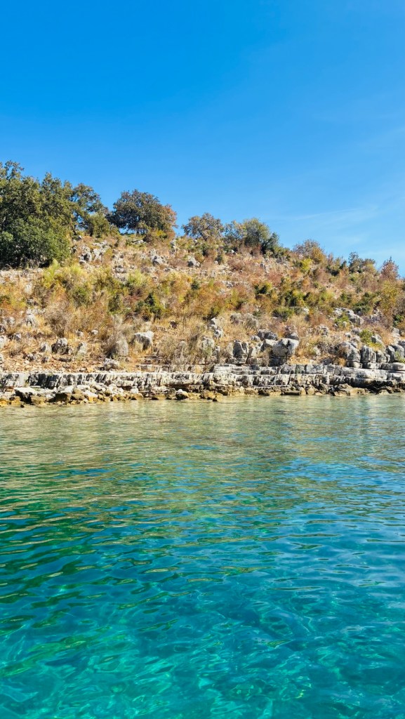 Vue d'une côte rocheuse surplombant une eau turquoise et un ciel bleu clair.