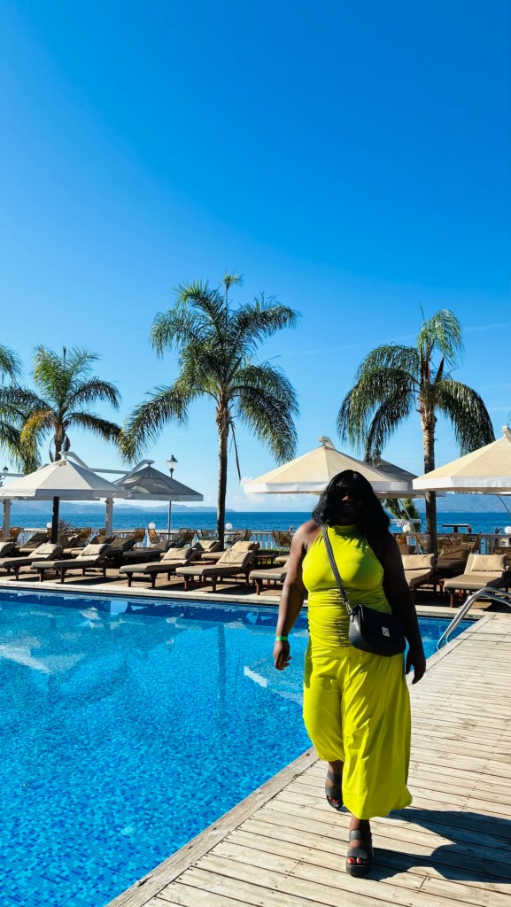 Une personne marchant le long d'une piscine avec des palmiers dans un environnement ensoleillé, portant une tenue jaune vif.