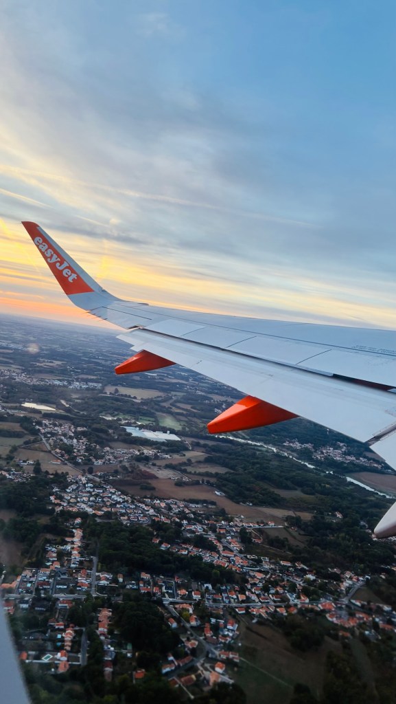 Vue d'un aile d'avion easyJet survolant des paysages avec un coucher de soleil et des habitations en dessous.