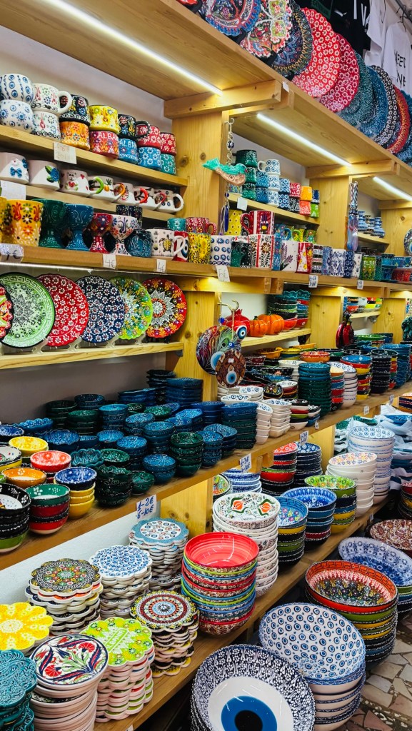 Étals remplis de vaisselle colorée, y compris des tasses, assiettes et bols, sur des étagères en bois.